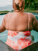 Femme ronde de dos assise dans une piscine avec un maillot une pièce imprimé corail 
